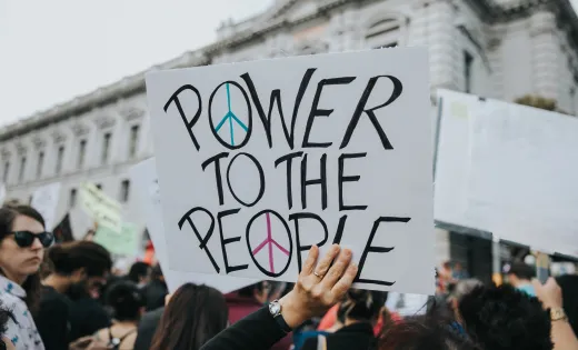 Photo of a demonstrator holding up a sign that reads "Power to the People"