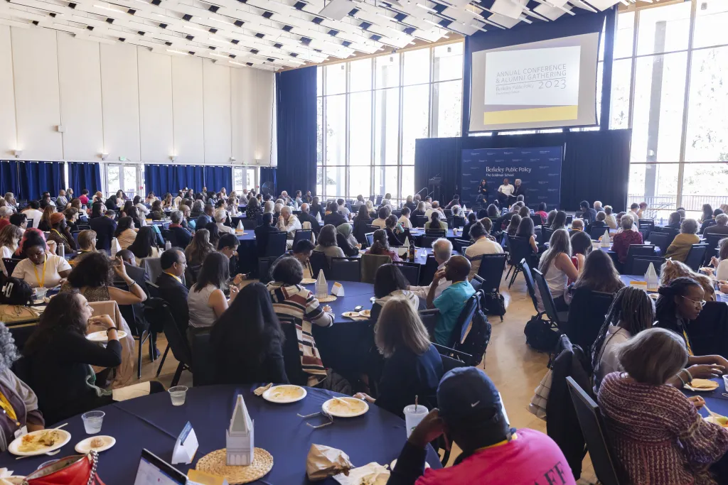 Large audience seated at round tables in a conference hall, listening to speakers on stage at the Berkeley Public Policy Annual Conference and Alumni Gathering 2023.