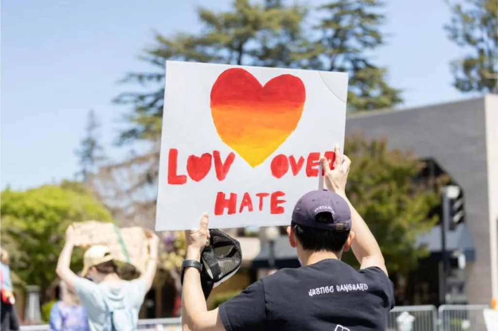 Photo of a demonstrator holding a sign that reads "Love Over Hate"