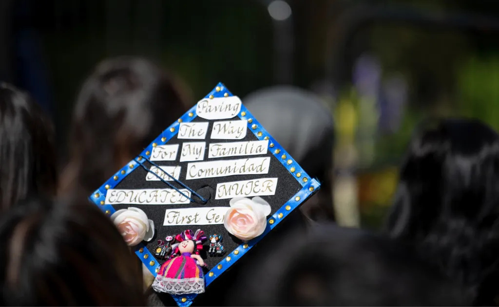 Closeup of a graduation cap that reads "Paving the way for my familia and comunidad. Educated mujer first gen"
