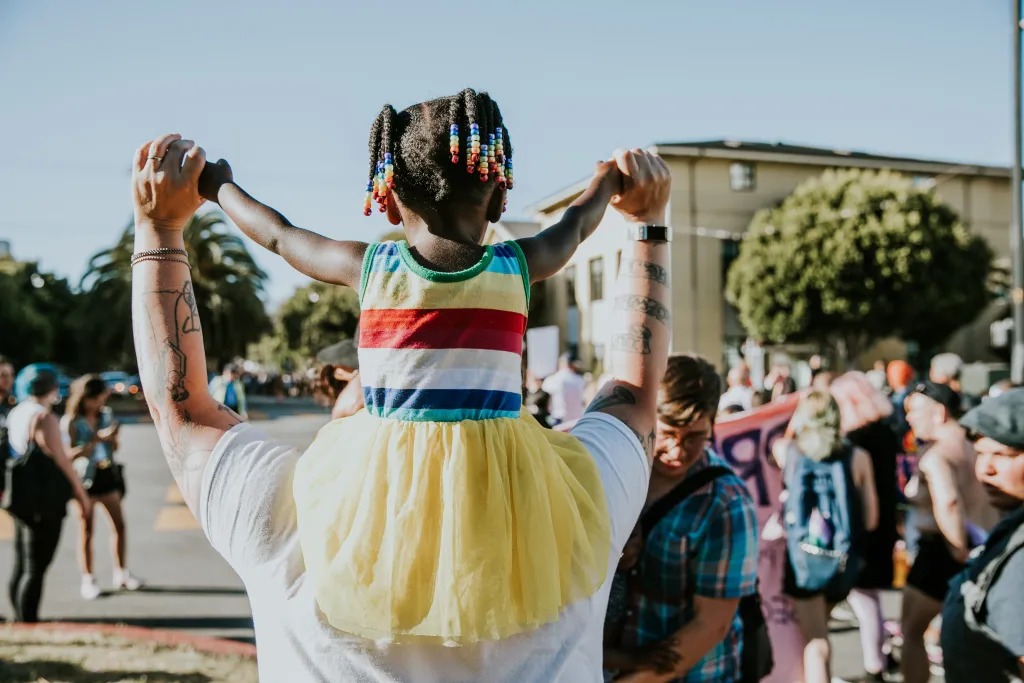 Child on adult's shoulders, wearing rainbow colors at 2018 Pride March