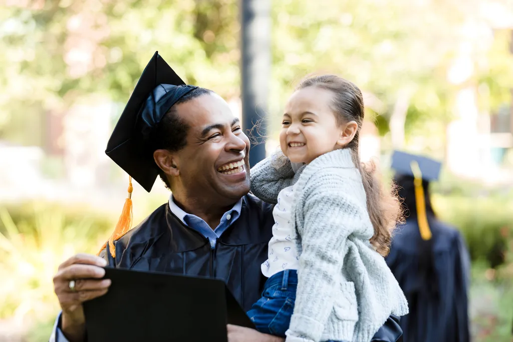 An adult student celebrating his graduation with his daughter
