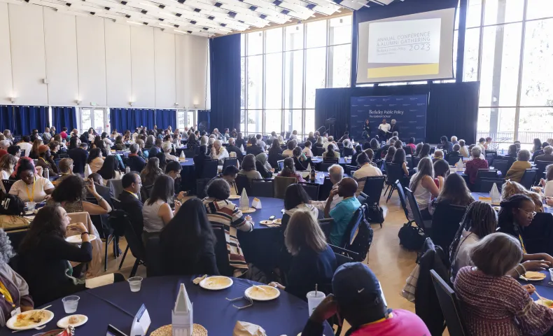 Large audience seated at round tables in a conference hall, listening to speakers on stage at the Berkeley Public Policy Annual Conference and Alumni Gathering 2023.