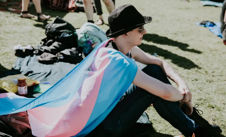 Person sitting on grass with trans flag