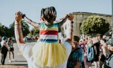 Child on adult's shoulders, wearing rainbow colors at 2018 Pride March