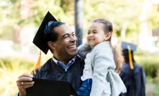 An adult student celebrating his graduation with his daughter