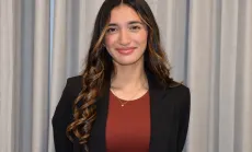 Natalia Medina smiling at the camera, with long, wavy brown hair, wearing a black blazer over a rust-coloured top and a delicate gold necklace.