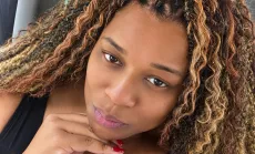 Close-up portrait of Shay with her chin resting on her hand, framed by highlighted curls.