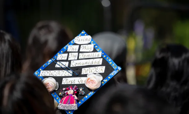 Closeup of a graduation cap that reads "Paving the way for my familia and comunidad. Educated mujer first gen"