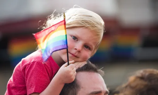 All Children Matter. young girl riding dad's shoulder holding rainbow flag