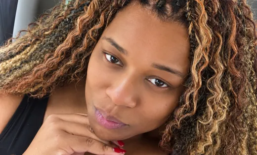 Close-up portrait of Shay with her chin resting on her hand, framed by highlighted curls.