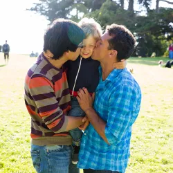 Two fathers embrace their son on a green lawn