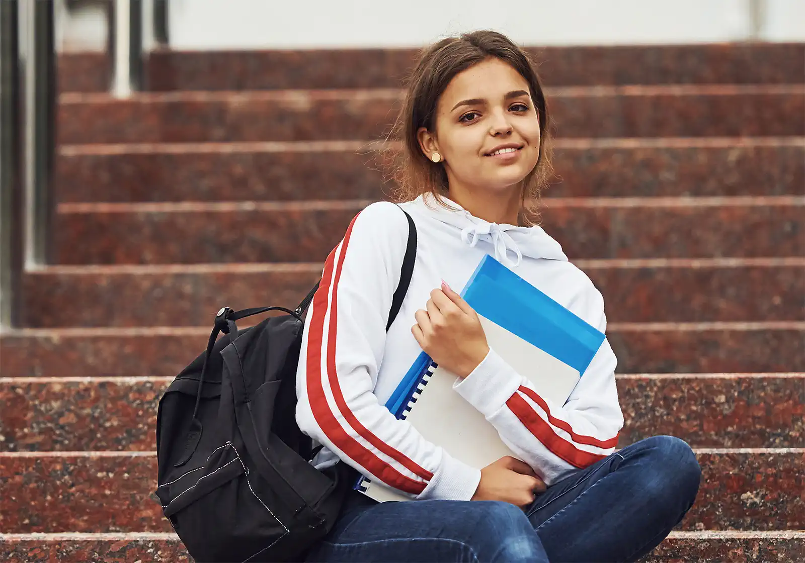 Female student sitting on stairs outdoors with documents